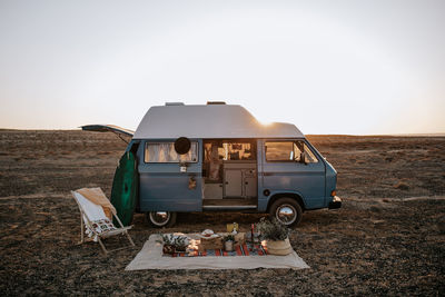Blanket with various food for picnic placed near parked van in savanna against sunset sky