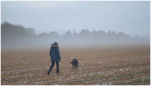 Rear view of woman with dog walking on field during winter