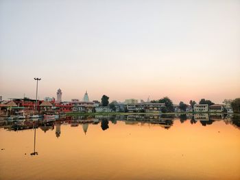 Buildings by river against sky during sunset