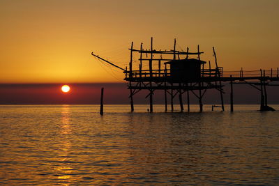 Silhouette built structure on sea against sky during sunset