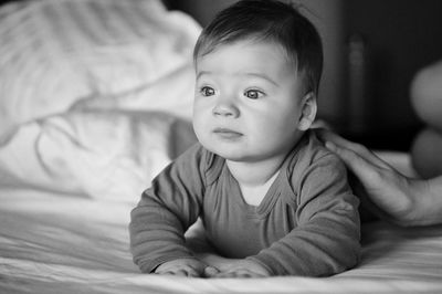 Cute baby looking away while lying on bed at home