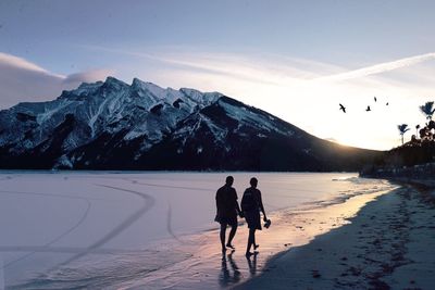 People on beach against sky during sunset