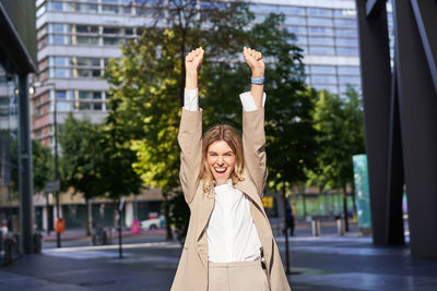 Portrait of young woman with arms raised in city