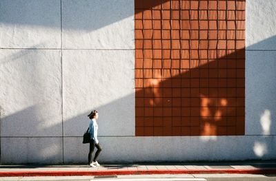 Full length of man walking against building in sunny day