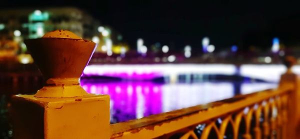 Close-up of illuminated railing by river in city at night