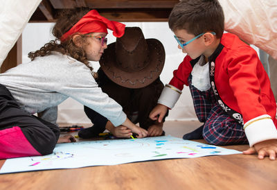 Children wearing costumes coloring paper on hardwood floor