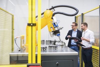Engineers with tablet pc examining robotic arm in factory