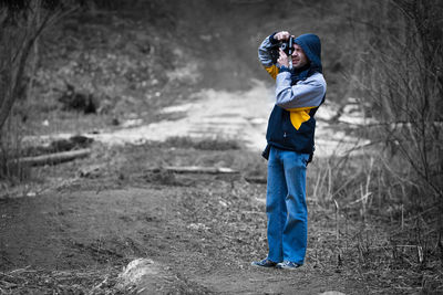 Side view of man photographing with camera while standing on field