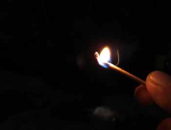 Close-up of hand holding lit candle in the dark