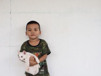 Portrait of cute boy with cat against white wall