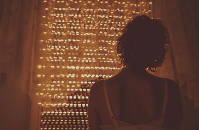 Rear view of woman looking at illuminated window