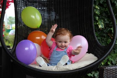 Smiling girl with balloons sitting on chair at yard