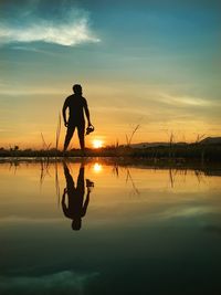 Silhouette man on lake against sky during sunset