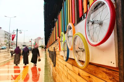 Colorful wheels on wall with people walking on sidewalk in city