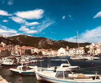 Sailboats moored in harbor by city against sky