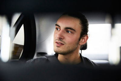 Close-up of thoughtful young man looking through window while riding car