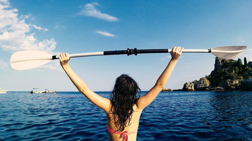 Rear view of woman with arms raised in sea against sky