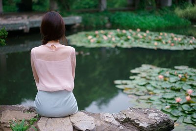 Rear view of woman sitting on rock by lake