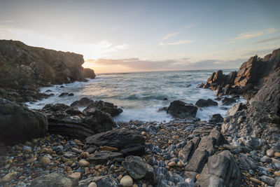 Scenic view of rocky shore and sea against sky during sunset