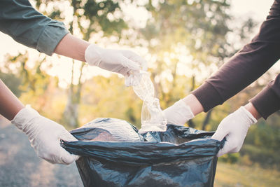 Cropped hand wearing protective glove while putting plastic bottle in bag