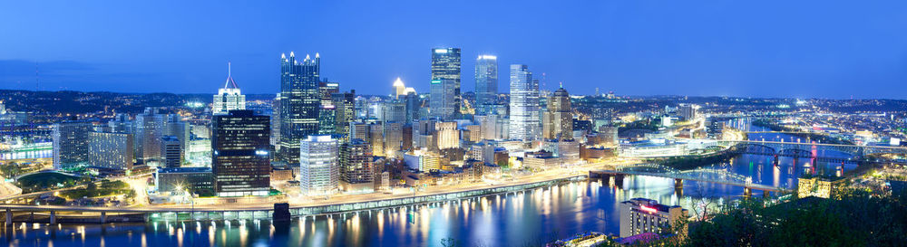 Illuminated buildings by river against sky in city at night