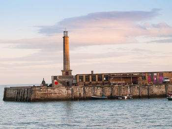 Lighthouse on sea against buildings