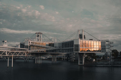 Bridge over river by buildings against sky at dusk