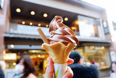 Cropped hand holding ice cream cone against built structure