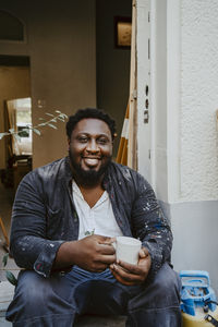 Portrait of smiling male carpenter holding having coffee at doorway of house