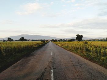 Road amidst field against sky