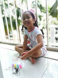 Portrait of smiling cute girl holding paintbrush while sitting in balcony at home