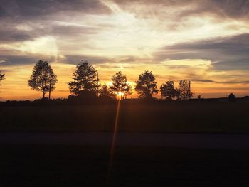 Silhouette trees on landscape against sky at sunset