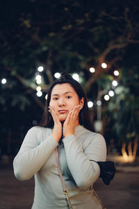 Portrait of young woman standing against illuminated christmas tree