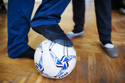 Low section of man leg with football while standing on wooden floor