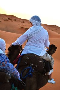 Rear view of man sitting on camel in desert