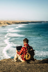 Rear view of woman sitting at beach against clear sky