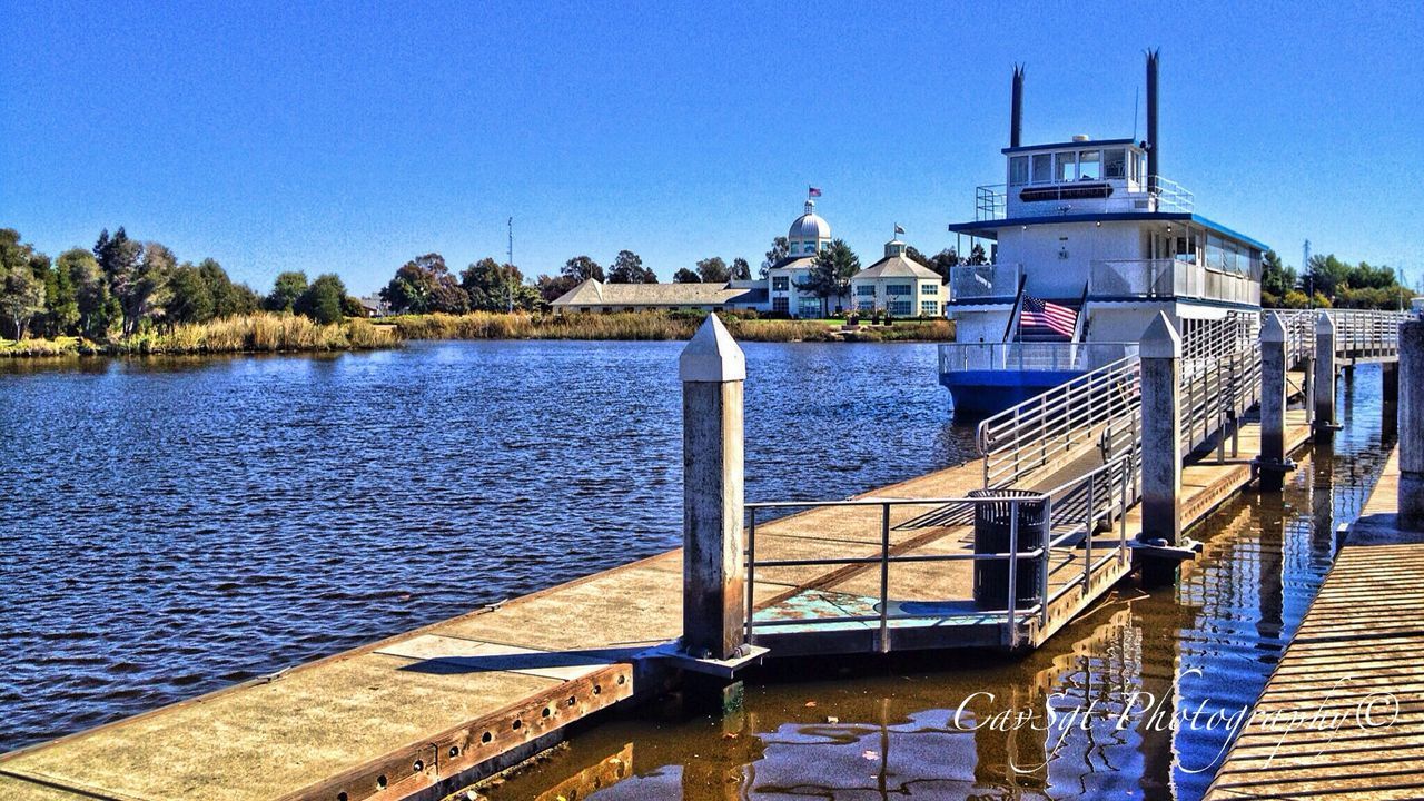 clear sky, blue, water, copy space, built structure, architecture, building exterior, river, rippled, sunlight, pier, lake, transportation, railing, nature, day, tranquil scene, tranquility, outdoors, nautical vessel