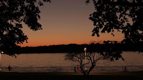 Silhouette trees by lake against sky during sunset