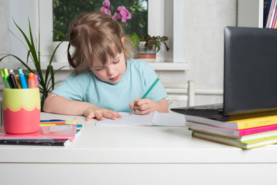 Girl sits at a table with books and a notebook and does her homework. children learning at home.