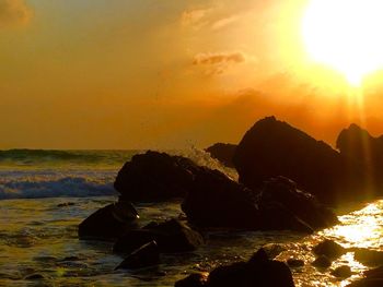Rocks on beach against sky during sunset