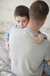 Man carrying sad boy on bed at home