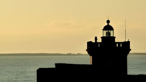 Lighthouse by sea against sky during sunset