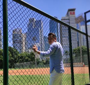 Man standing by chainlink fence against sky
