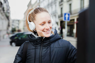 Smiling young woman using parking meter while standing on footpath