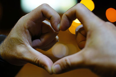 Cropped hands of people making heart shape over defocused lights at night