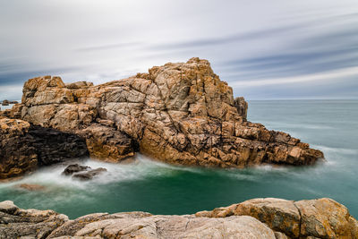 Rock formation on sea shore against sky