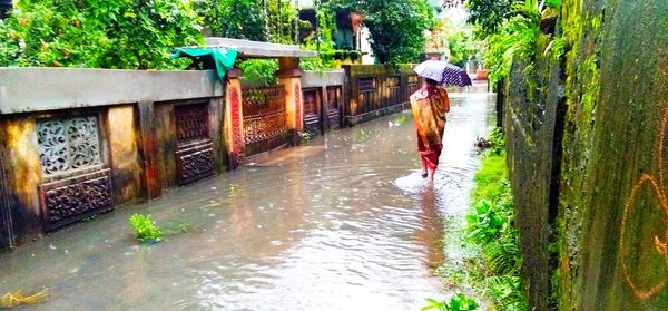 Full length of man with umbrella in canal during rainy season