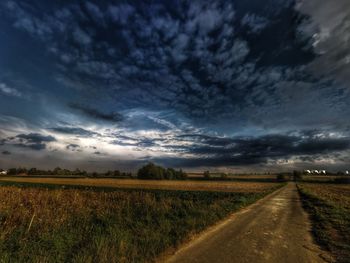 Road passing through field against cloudy sky