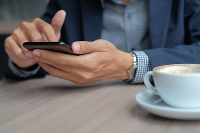 Midsection of man holding coffee cup on table