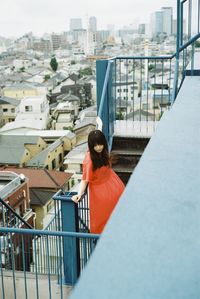 Rear view of woman standing on railing against buildings